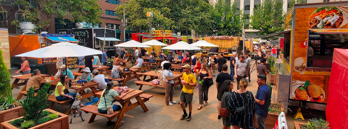 A large and busy food cart pod with picnic tables for outdoor seating.