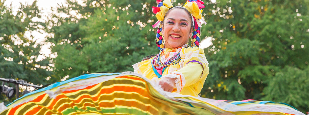 Woman wearing yellow dress with colorful flair smiles as she dances.