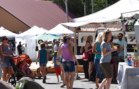 People browsing vendor booths and shopping at an outdoor art fair on a sunny day.