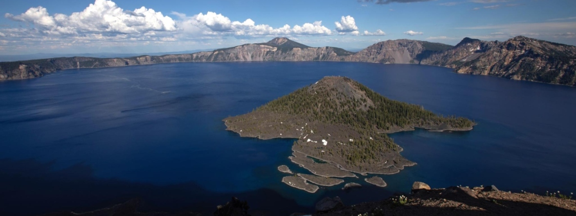 Large blue lake in a caldera with a small island in the middle, blue sky and white clouds.