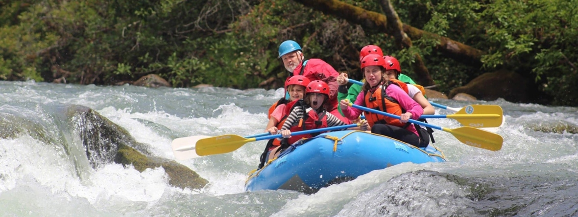 A raft full of people travels over a river rapid.