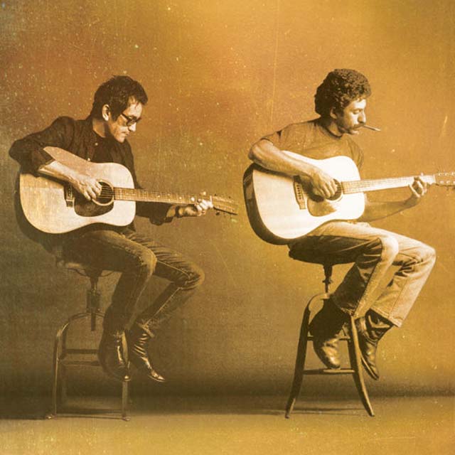 Two men sitting on stools playing guitar.