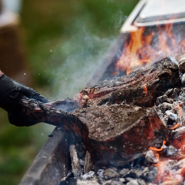 Large steaks being cooked over a fire.