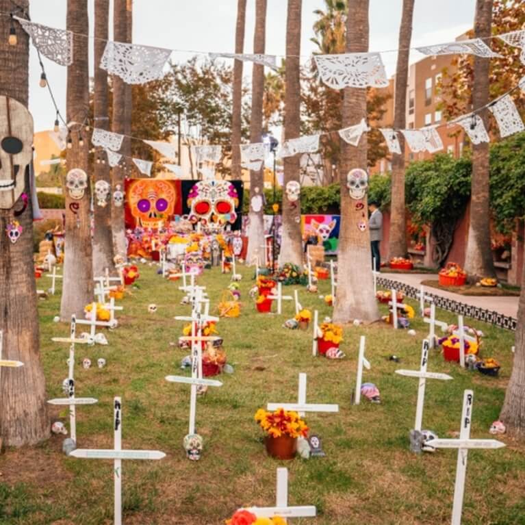 Colorful Día de los Muertos altars with marigolds set up in an outdoor plaza.