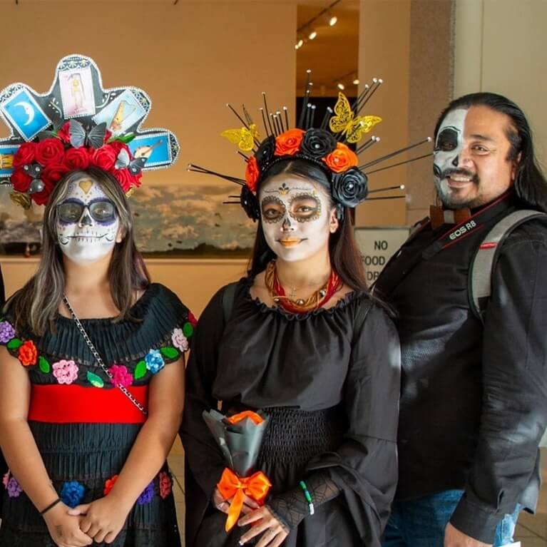 People with painted calavera faces smiling during a Día de los Muertos celebration.