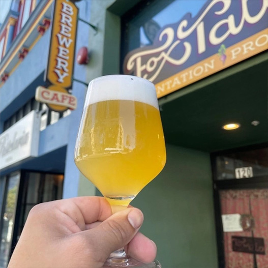 A person holding up a beer outside of Fox Tale.