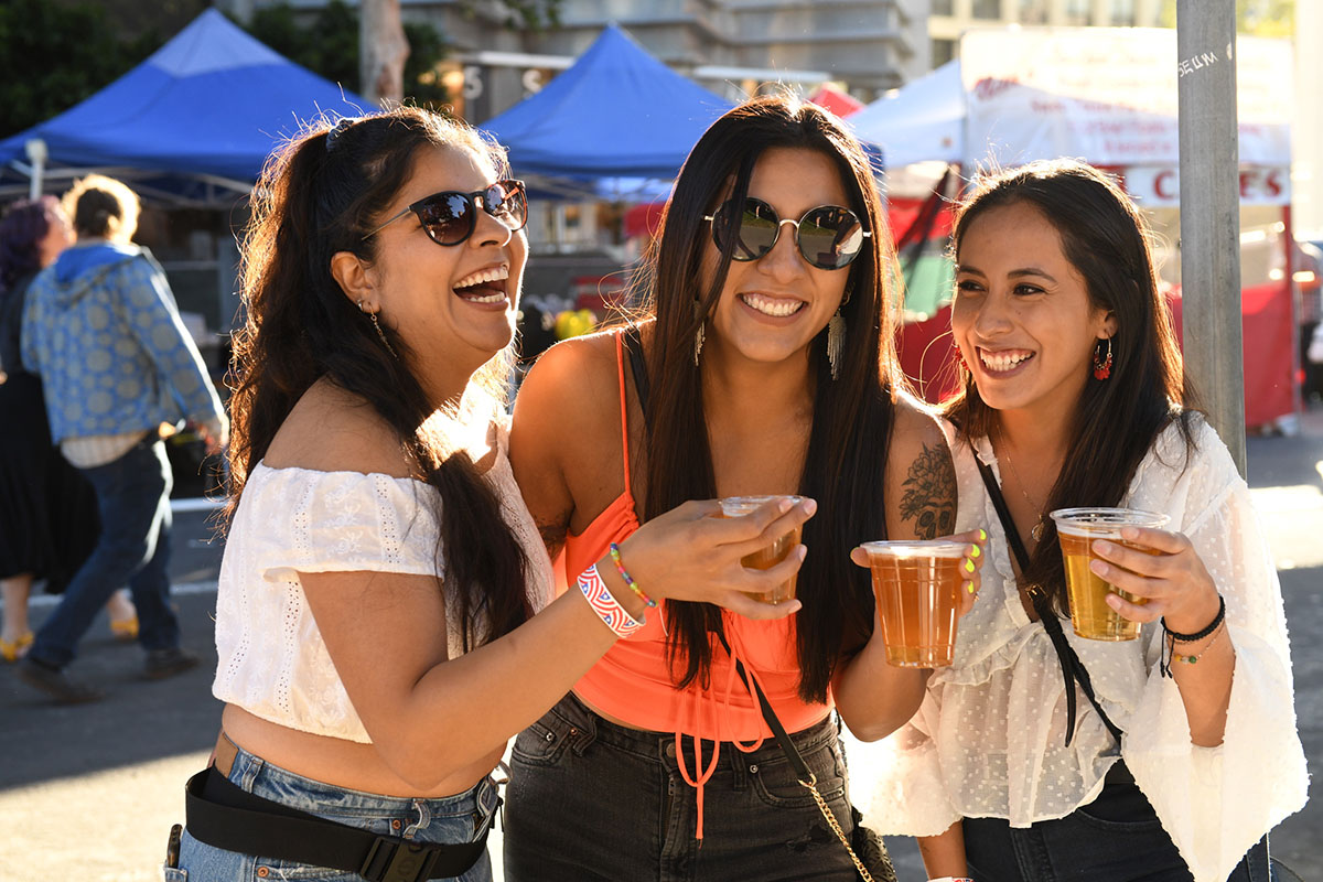 Three women share drinks during a street festival.