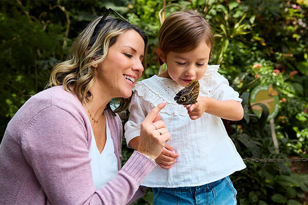 a mother and child looking at a butterfly perched on the child's finger