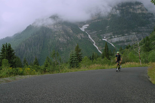 a bicyclist riding on a road with a mountain rising into the fog behind him