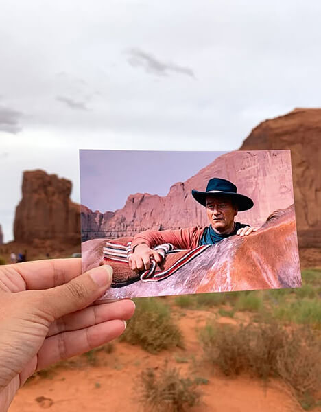 an old photo of john wayne in "the searchers" held up against a backdrop of the rock formations in the photo