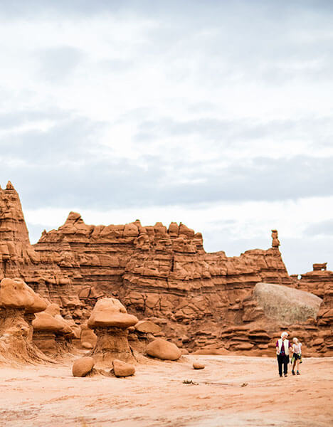 two people walking in the desert near hoodoo rock formations