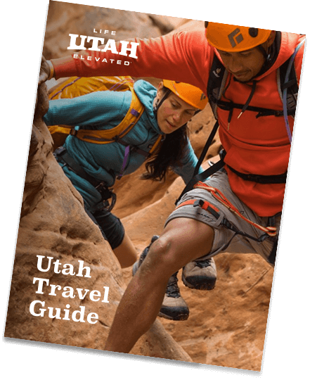 a cover of a utah travel guide with an image of a man and woman climbing through a canyon on it