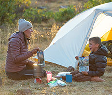 a woman and child sitting on the ground outside of a tent