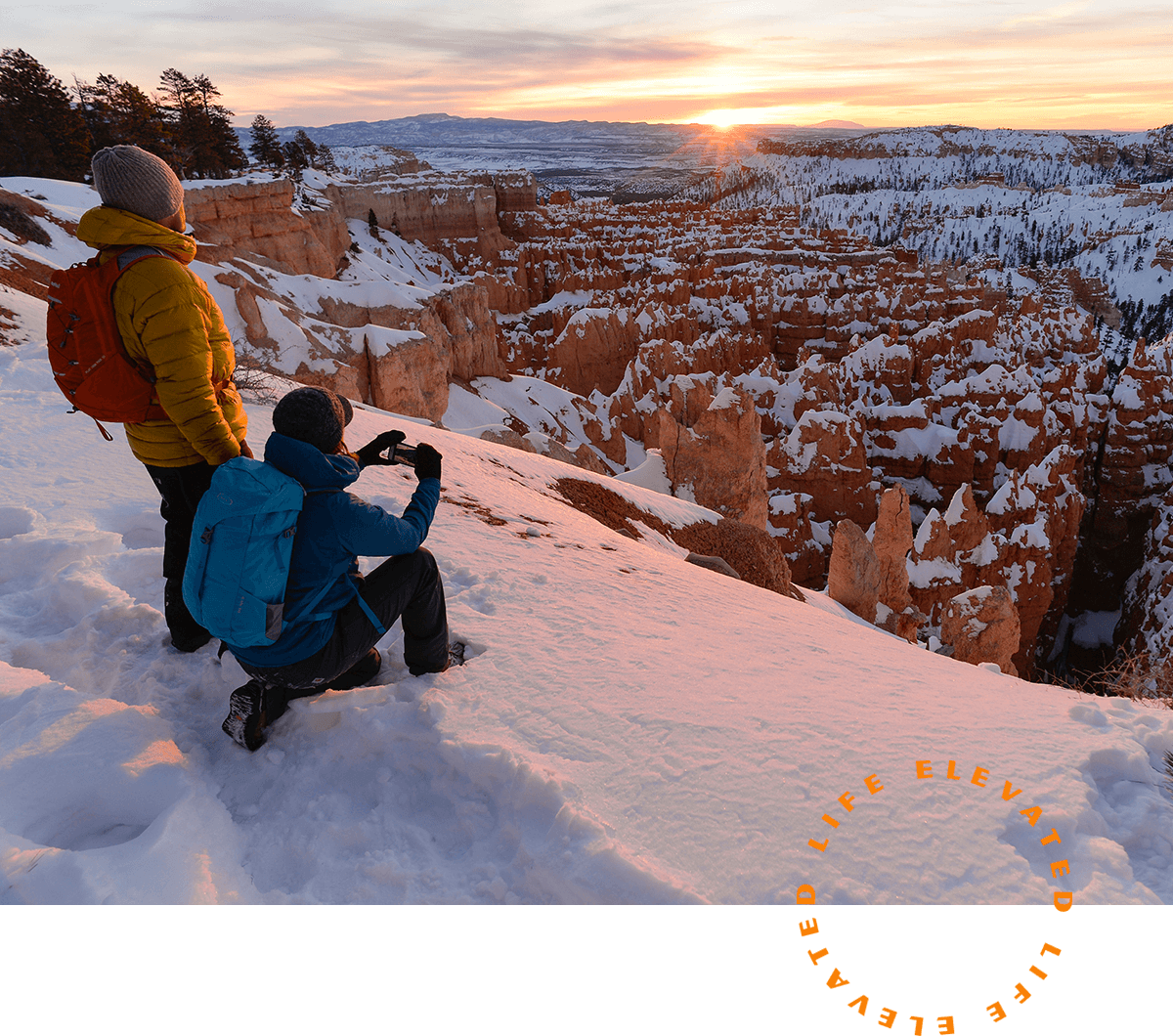 a man taking a picture of the sunset over a snowy canyon