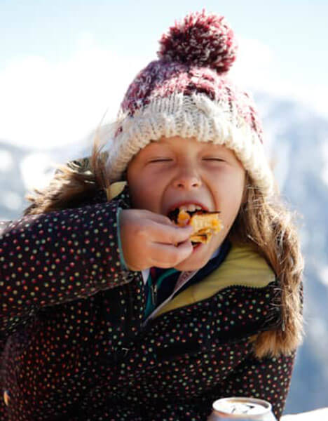 a little girl eating a piece of food in the snow