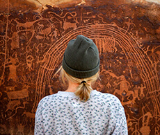 a woman with a knit cap standing in front of a petroglyph