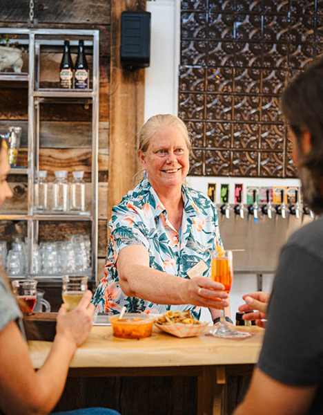 an older woman holding a drink at a bar