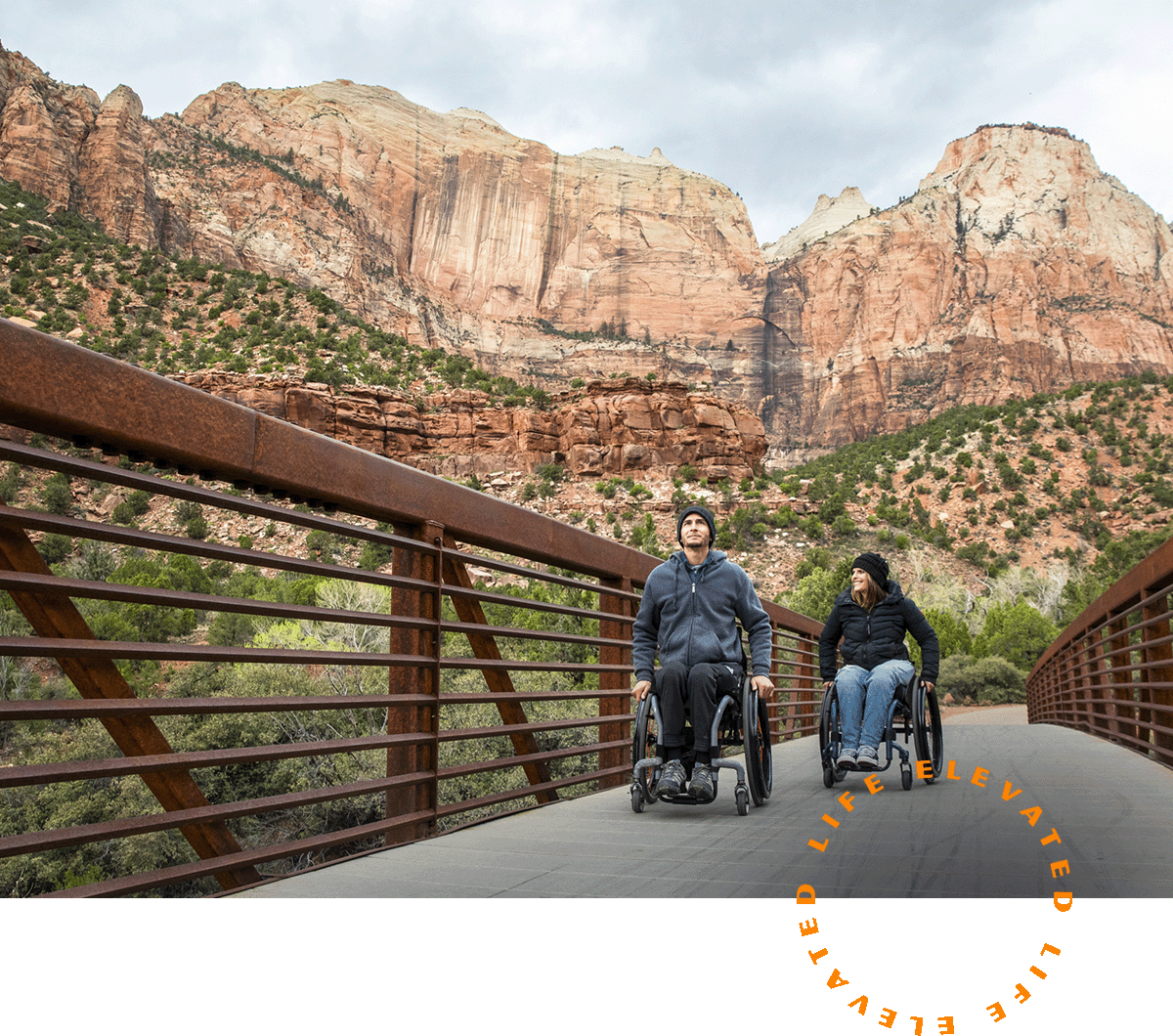 Two people in wheelchairs going across a bridge.
