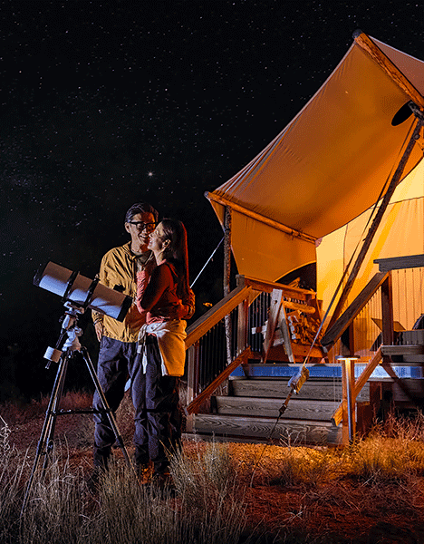 A couple with a telescope stargazing at a night sky