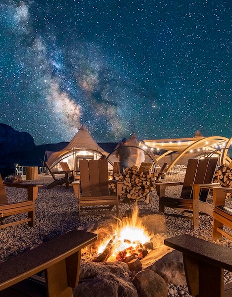 chairs and canvas tents around a campfire with a backdrop of a starry sky