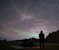 a man standing in a field looking at the night sky and pointing lasers at stars