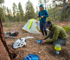 two people setting up their tents in the woods