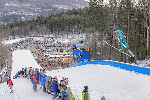 A crowd watches as a ski jumper launches from the top of a jump. 