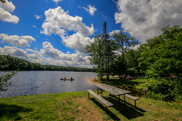 Two people paddle canoes seen from a distance on a lake on a clear summer day.  