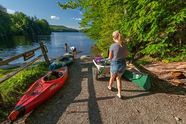 Two people load canoes into the water at a boat launch outside in the summer at a lake.  