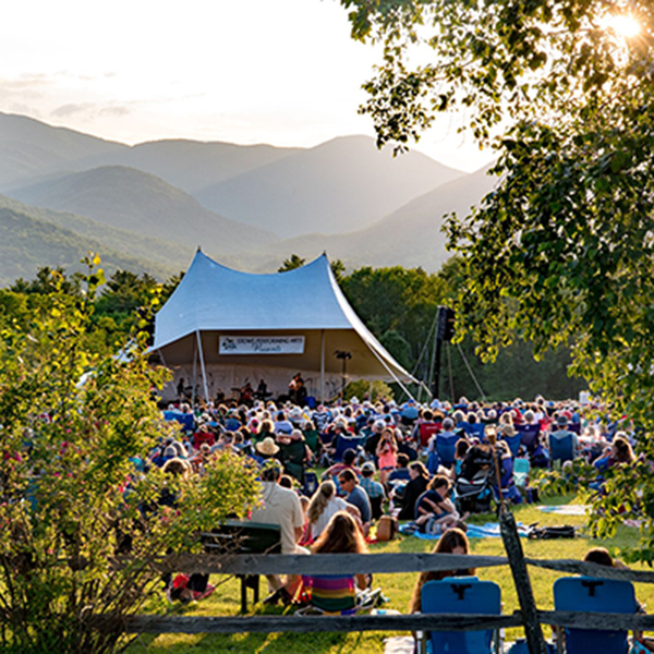 People crowd at an outdoor live music event with mountains in the background.&nbsp;&nbsp;