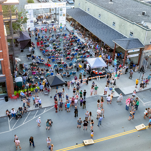 People seen from high above in an aerial image walk throughout a street festival with vendors and a stage set for live music.&nbsp;