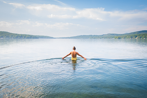 A person seen from behind in waist-deep water in a lake on a summer day.  