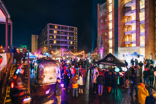 A bustling crowd celebrates outdoors on a winter night, with bright lights creating a festive ambiance.