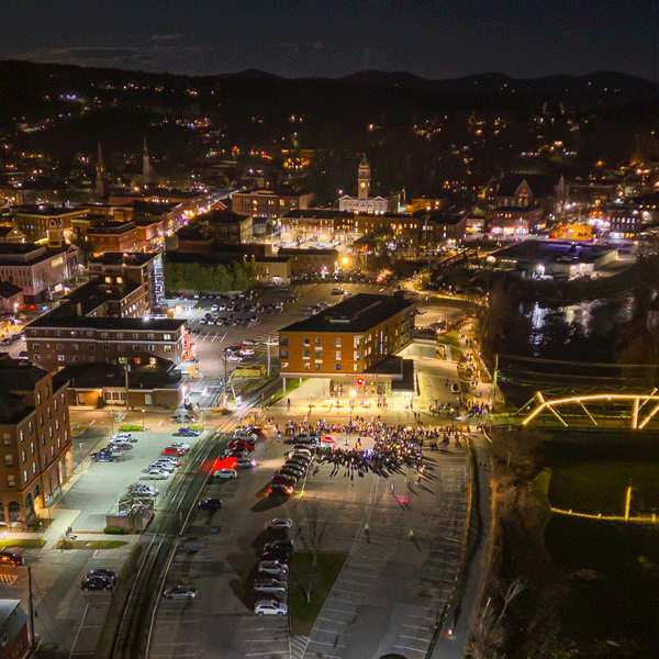 Seen from above at night, a historic downtown with bridges illuminated with festive lights. 