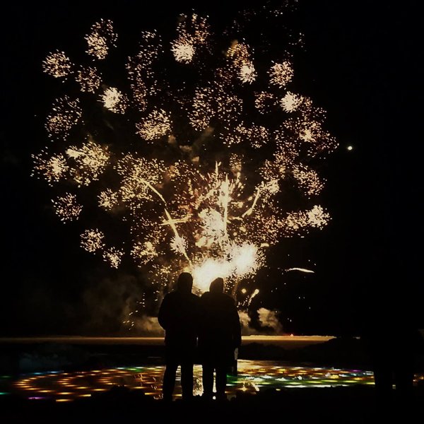  Two people, seen from behind in silhouette, watching a fireworks display at night.&nbsp;