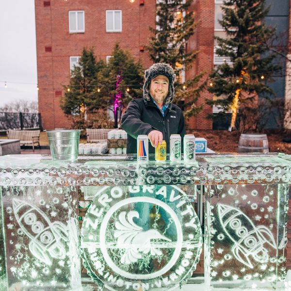 A person behind a bar made of ice, smiling and serving drinks. 
