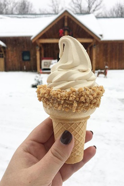 A hand holds up a white, soft ice cream cone with crunchy toppings outside in winter. 