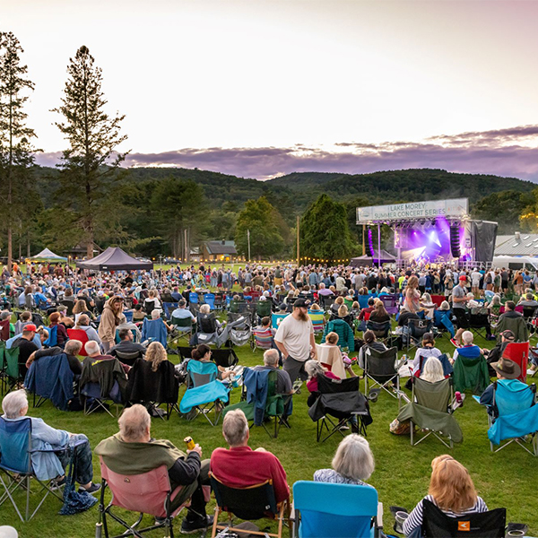 A crowd gathers outside to watch live music in a bandshell outside on a summer evening.&nbsp;