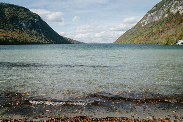 A lake in the summer with clear water and mountains on either side in the background.