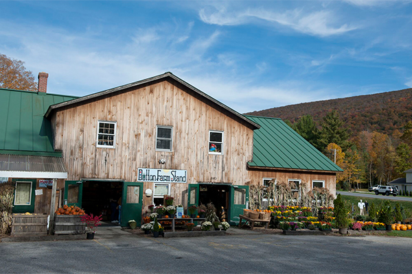A weathered barn with a sign reading “Dutton Farmstand” and a selection of flower, produce, and more for sale. 