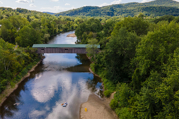 A covered bridge seen from above in the summer spanning a river on a sunny day.