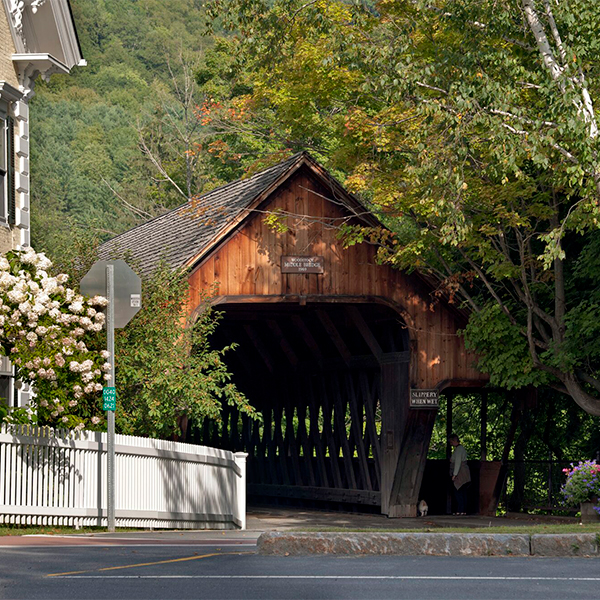A covered bridge in the summer with flowers blooming around the entrance on a sunny day.