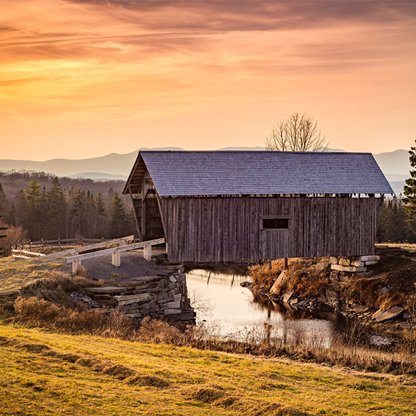 A scenic covered bridge at sunset, surrounded by mountains.