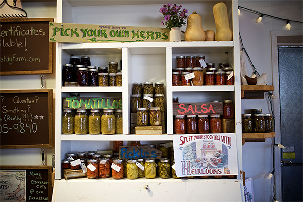 Jarred and canned produce on shelves indoors with a sign reading “Pick Your Own Herbs.”