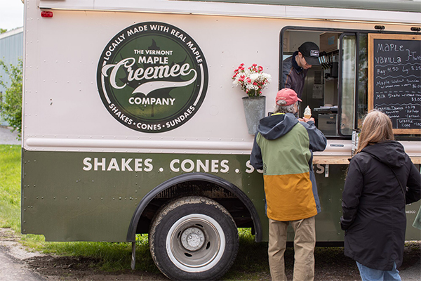 People wait in line at a food truck outside on a rainy day serving ice cream. 