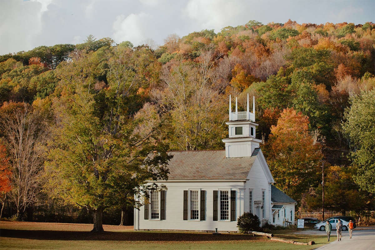 A historic white building surrounded by trees with fall leaves outdoors in Vermont in autumn. 