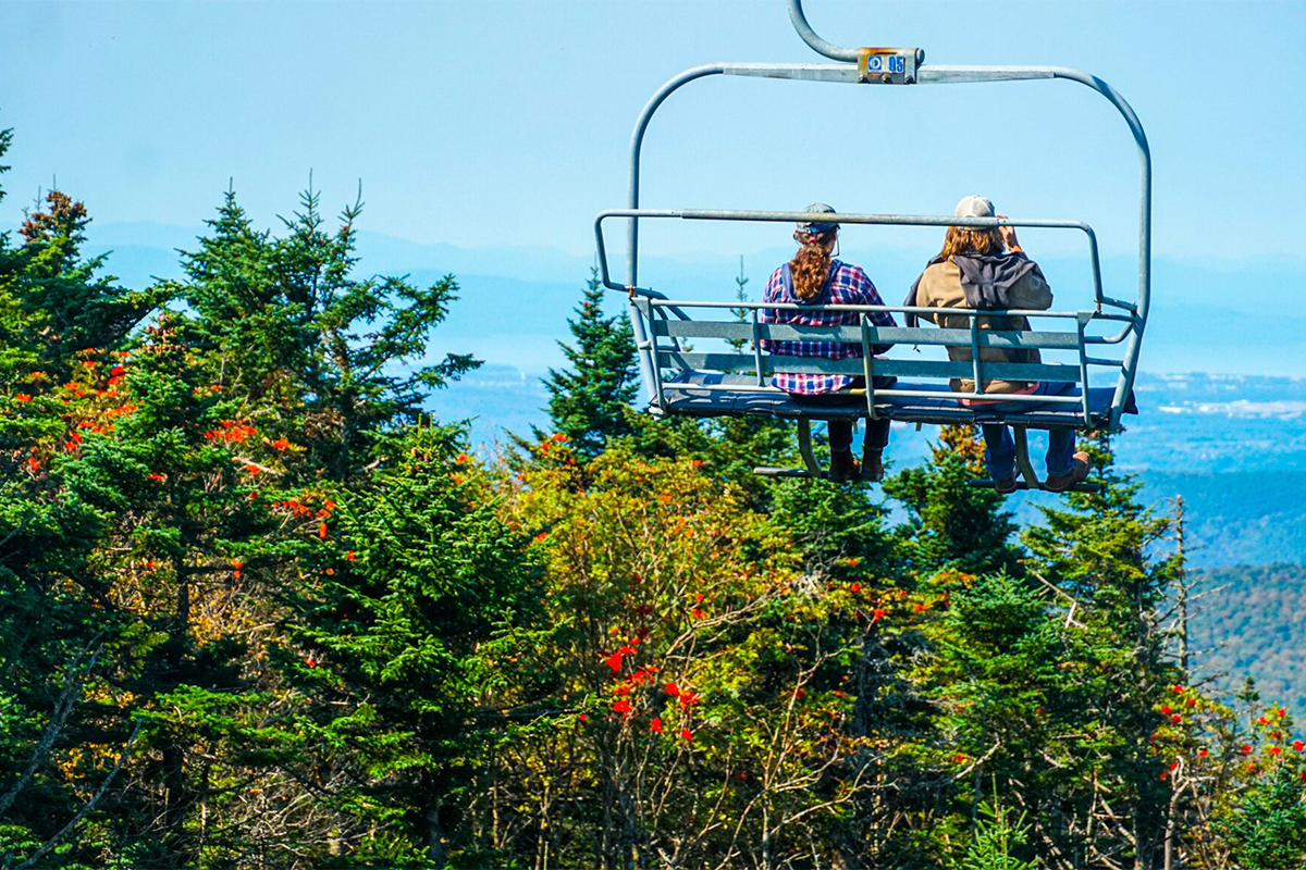 Two people on a scenic chairlift ride see fall foliage from above. 