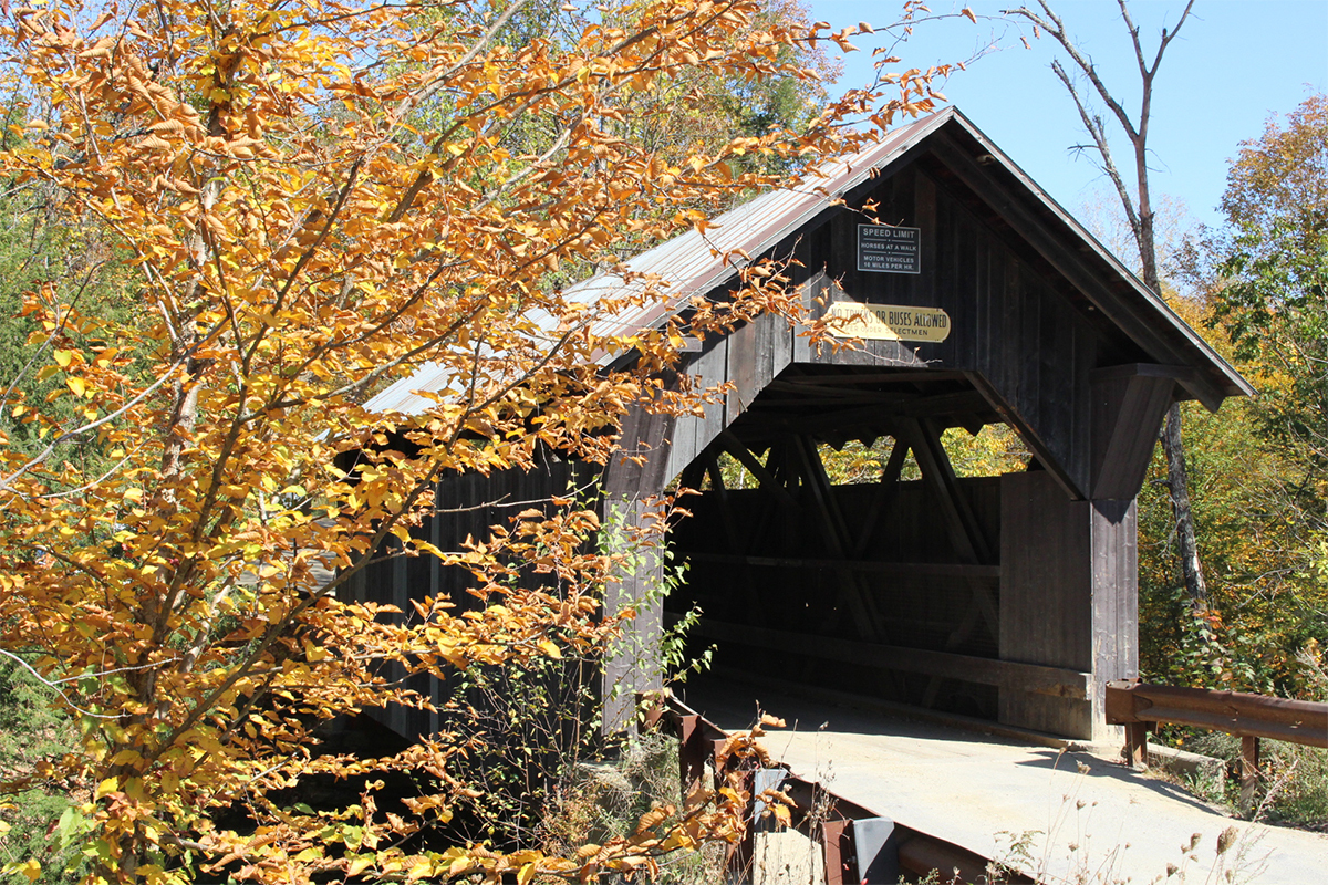 Historic wooden covered bridge surrounded by vibrant golden autumn foliage.