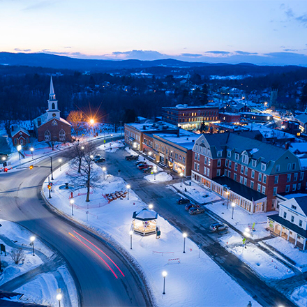  From overhead, a town blanketed in snow at dusk with lights glowing. 
