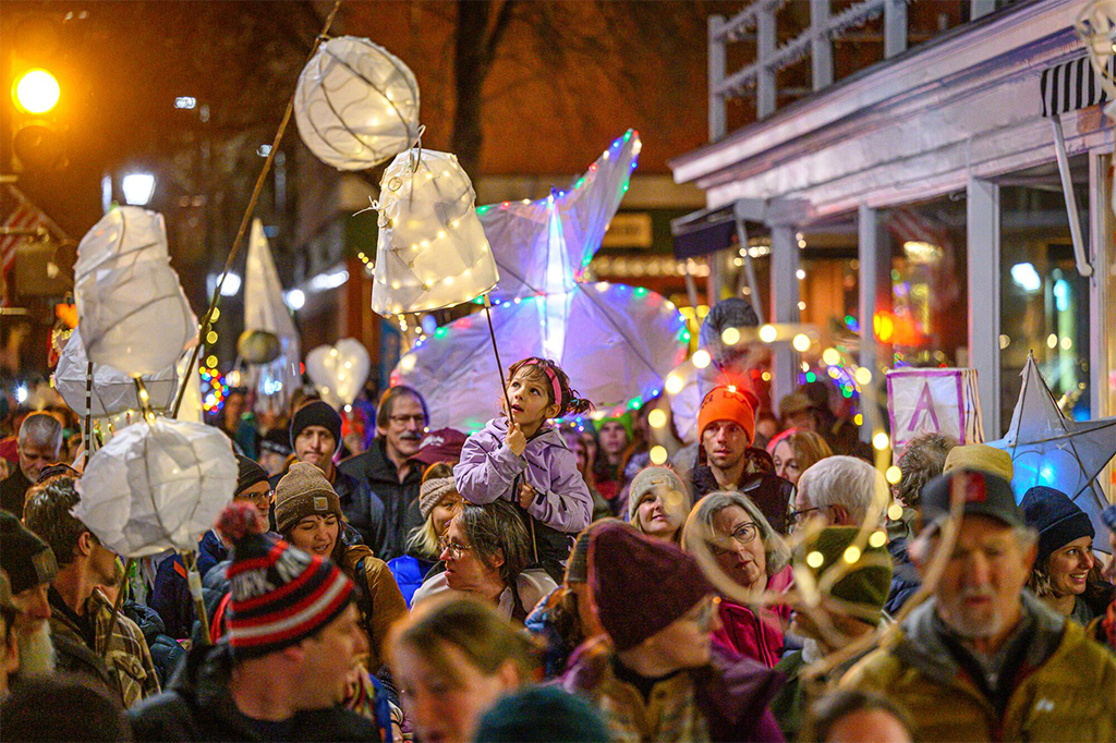 A crowd of people holding paper lanterns in a street at night.